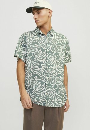 Camisa de manga corta en verde con patrón de hojas blancas, hecha de tela ligera. Presenta un cuello abotonado y un corte relajado.