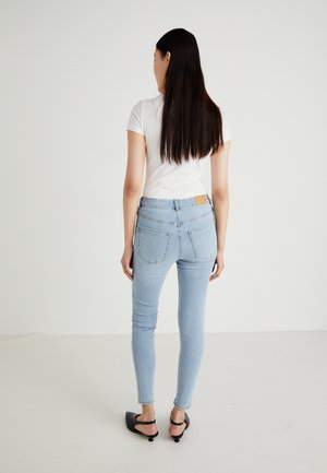 Jean skinny bleu clair avec une taille mi-haute, design à cinq poches et une étiquette en cuir marron à l'arrière de la taille.