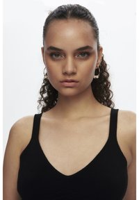 Zwarte tanktop met een V-hals ontwerp en dikke banden, met een gladde textuur. Model heeft krullend haar en kleine ringoorbellen met accenten.
