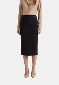 Gonna a matita nera con cuciture verticali e una texture liscia, abbinata a una camicia beige con bottoni. Presenta un sottile accento metallico in vita.