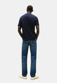 Maglietta navy a maniche corte abbinata a jeans di denim blu. I jeans presentano tasche posteriori e discreti dettagli di cucitura. Sneakers completano il look.
