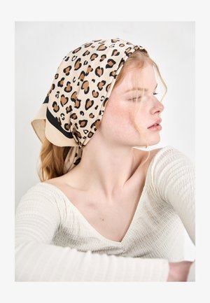 Leopardenmuster Seidentuch in Beige mit schwarzen Akzenten, mit einer glatten Textur und einer dreieckigen Form, hinten am Kopf gebunden.