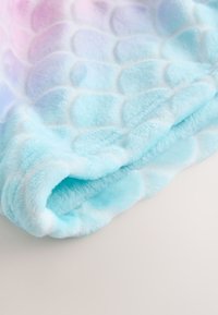 Svetlo modra plišasta odeja z mehko, teksturirano površino, ki ima iridescentni vzorec lusk v pastelnih barvah. Zaobljeni robovi, trpežen material.