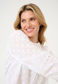 Witte katoenen blouse met gestructureerde patronen en kantafwerking op de mouwen. Het ontwerp heeft een knoopsluiting en een losse pasvorm.