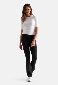 Hvit tettsittende t-skjorte med korte ermer, kombinert med svarte flagrende leggings. Materialet virker elastisk; antrekket er egnet for trening.