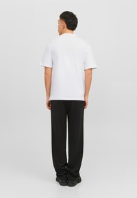 White short-sleeve t-shirt paired with black loose-fitting pants, featuring a smooth finish and relaxed fit, viewed from the back.