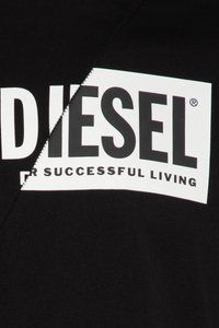 Juodos medvilnės audinys su dideliu baltu stačiakampiu logotipu, kuriame juodomis riebiosiomis raidėmis parašytas žodis „DIESEL“, o po juo mažesnėmis raidėmis matomas šūkis.