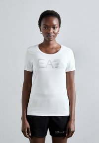 T-shirt bianca a maniche corte con scollo rotondo, decorata con il testo argentato "EA7" e "EMPORIO ARMANI" impreziosito da piccoli strass.