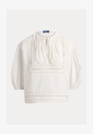Blusa bianca a maniche lunghe con dettagli in pizzo quadrato, scollo arricciato con chiusura a laccio ed elastici ai polsi.