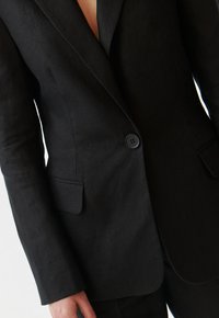 Černý lněný blazer s jedním knoflíkem, s klopami a decentní texturou, obsahující detail přední kapsy.