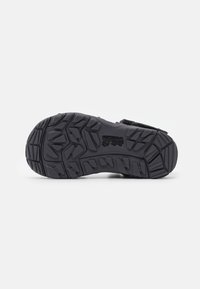 Black outdoor shoe sole with a textured rubber surface, featuring deep treads for grip and a cushioned design for comfort.