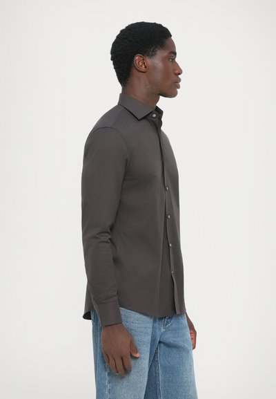 Mørk grå langermet skjorte med krage og knapper, glatt tekstur og tilpasset passform. Kombinert med lyseblå denimjeans.