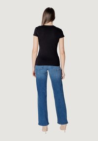 Maglietta nera attillata a maniche corte abbinata a jeans larghi a vita alta di colore blu chiaro. Tessuto liscio, design informale e minimalismo nei dettagli.