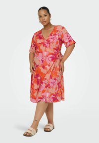 Wrap dress in coral-pink with floral pattern featuring large pink and orange blossoms. Short sleeves and adjustable tie at the waist.