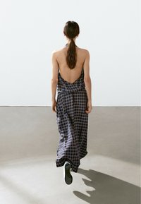 Long, sleeveless plaid dress in dark blue and black with a low back and loose fit, draping to the floor. Minimalist design with soft texture.