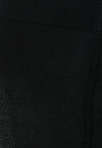 Pantys negras con una textura suave, que presentan un sutil brillo y costuras reforzadas. La tela parece elástica y ajustada al cuerpo.