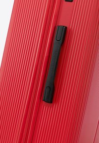 Valigia rigida rossa con texture a righe verticali, dotata di maniglia e zip neri. Include il marchio sulla maniglia.