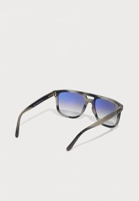 Ochelari de soare cu o ramă gri translucid, lentile albastre cu degradé și temple drepte, elegante. Prezintă accente metalice și o marcă subtilă.