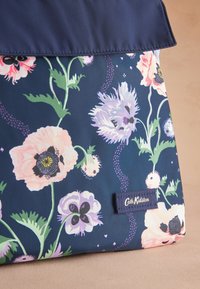 Květinová taška přes rameno s tmavě modrým pozadím, růžovými a fialovými květinami, zelenými listy a textilní štítkem s nápisem "Cath Kidston".