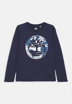 Marineblå langærmet skjorte med et rundt jordlogo med et træ og ordene "Timberland Nature Needs Heroes."