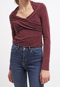 Bordeaux långärmad topp med samlad frontdesign och V-halsringning. Matchad med hög midja blå jeans. Mjukt tyg med lätt struktur.