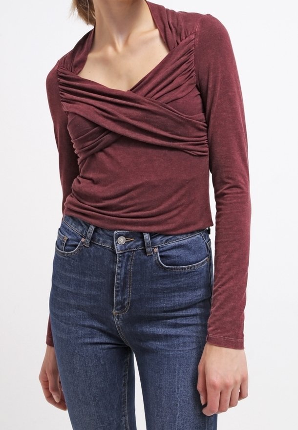 Bordeaux långärmad topp med samlad frontdesign och V-halsringning. Matchad med hög midja blå jeans. Mjukt tyg med lätt struktur.