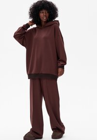 Bruine oversized hoodie met een tekstuurkap, gecombineerd met bijpassende wijde broek. Zacht materiaal met een relaxte pasvorm.