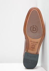 Semelle de chaussure en cuir marron avec un motif texturé. Présente un logo embossed "bugatti" et un design de bouclier. Taille 41. Bords renforcés pour plus de durabilité.