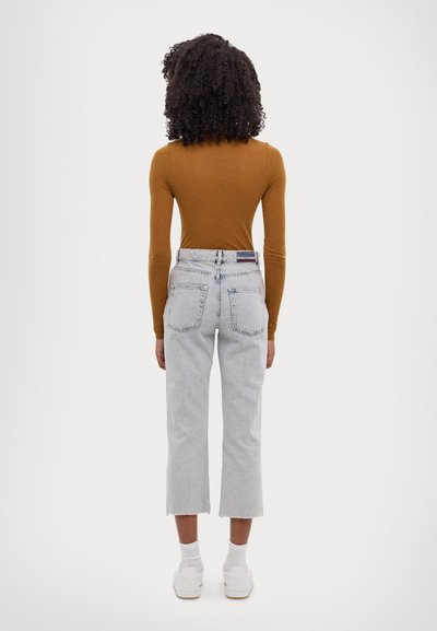 Piemērota brūna garām piedurknēm tops, gaiši izbalināti cropped džinsi ar plīsušu malu, baltas kedas, skatījums no aizmugures.