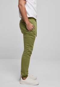 Grønne joggingbukser med tapered pasform, elastisk taljebånd og sidelommer. Kombineret med hvide sneakers for et afslappet look.