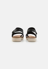 Sandales en cuir noir avec deux sangles réglables, une semelle intérieure beige clair et une semelle extérieure texturée beige avec un petit talon.