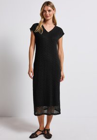 Abito midi lavorato a maglia di colore nero con scollatura a V, maniche corte e vestibilità ampia. Presenta un motivo a trama aperta e arriva all'altezza del polpaccio.