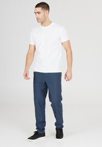 Vit t-shirt med kort ärm, kombinerad med mörkblå löst sittandebyxor, bärs med svarta sneakers. Enkel design med en mjuk textur.
