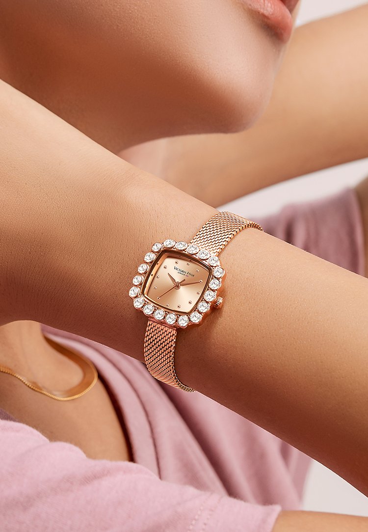 Rose gold nätarmbandsklocka för kvinnor med fyrkantig urtavla, omgiven av en kristallram och en minimalistisk urdesign. Armbandet har en fin nätstruktur.
