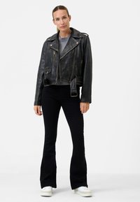 Svart läderbikerjacka med silverfärgade blixtlås, två framfickor och en figurnära design. Matchad med svarta utsvängda jeans och vita sneakers.