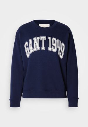 Tmavomodrá bavlnená mikina s okrúhlym výstrihom a dlhými rukávmi. Na prednej strane je nápis "GANT 1949" bielymi veľkými písmenami.