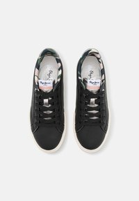 Mustat nauhavuorilla varustetut tennarit, joissa on sileä nahkapinta, kuvioitu kangasvuori ja valkoinen kumipohja. Hopeanväriset metallikoristeet nauhoissa.