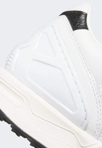 Zapatilla blanca con un acento texturizado negro, una superficie suave, un detalle geométrico elevado y una suela media blanca gruesa con una suela exterior negra.