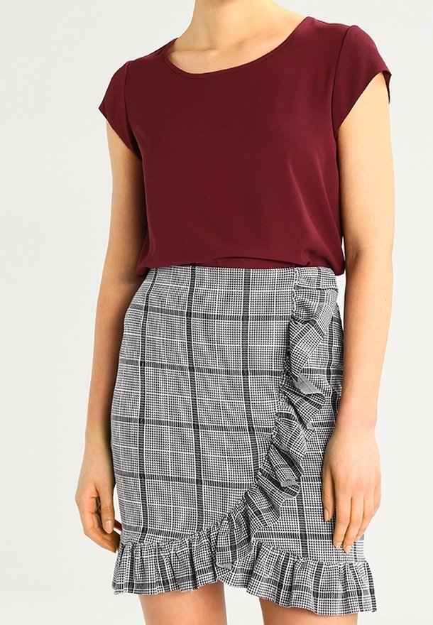 Femme portant un haut bordeaux à manches courtes et une jupe taille haute à carreaux noir et blanc avec des accents à volants.