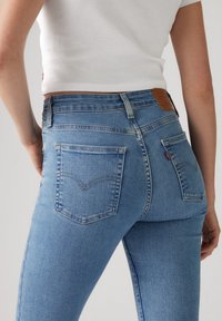 Jeans de mezclilla azul claro con cintura alta, diseño ajustado, bolsillos traseros con una costura de yugo curvada y una etiqueta de marca de cuero en la cinturilla.