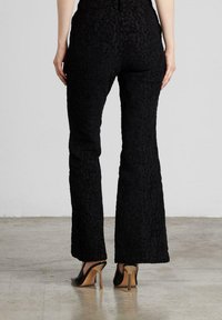 Pantalones negros acampanados con un patrón floral texturizado, con una cintura alta y una silueta ajustada, combinados con zapatos de tacón alto.