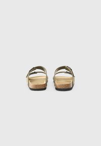 Sandales en suède vert avec deux sangles réglables, semelle en liège et semelle en caoutchouc. La vue arrière montre un design minimaliste et un talon ouvert.
