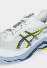 Λευκό και ανοιχτό γκρι παπούτσι τρεξίματος Asics με λευκά κορδόνια, σκούρο γκρι λογότυπο με νεον κίτρινο περίγραμμα και λεπτομέρειες στη σόλα σε ανοιχτό μπλε χρώμα.