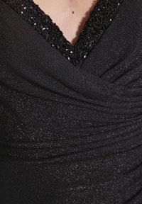 Schwarzes Kleid mit V-Ausschnitt, verziert mit schwarzem Perlenbesatz. Der Stoff hat eine schimmernde Textur und zeigt geraffte Details.