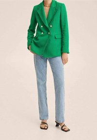 Zielona, teksturowana marynarka podwójnie zapinana z wyłami, połączona z jasnoniebieskimi jeansami prostymi i czarnymi sandałami na obcasie z paseczkami.