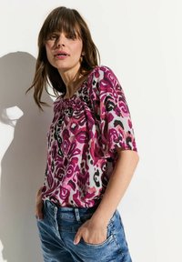 Blusa a maniche corte, con una fantasia viola e rosa, dal taglio rilassato, con scollatura arricciata e tessuto leggero e testurizzato.