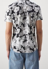 Camicia nera a maniche corte con un motivo floreale bianco, colletto classico e vestibilità rilassata. Tessuto di cotone con una consistenza morbida.