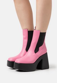 Botas de tobillo de cuero rosa con paneles elásticos laterales negros, suelas de plataforma gruesas negras y texturas contrastantes.