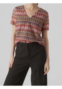 Haut à manches courtes et col en V présentant un motif zigzag multicolore en rouge, rose et noir. Confectionné en tissu léger et texturé.