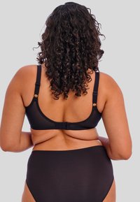 Soutien-gorge noir avec bretelles ajustables, fermeture à crochets et œillets, et texture lisse. Culottes noires taille haute complètent le design du soutien-gorge.